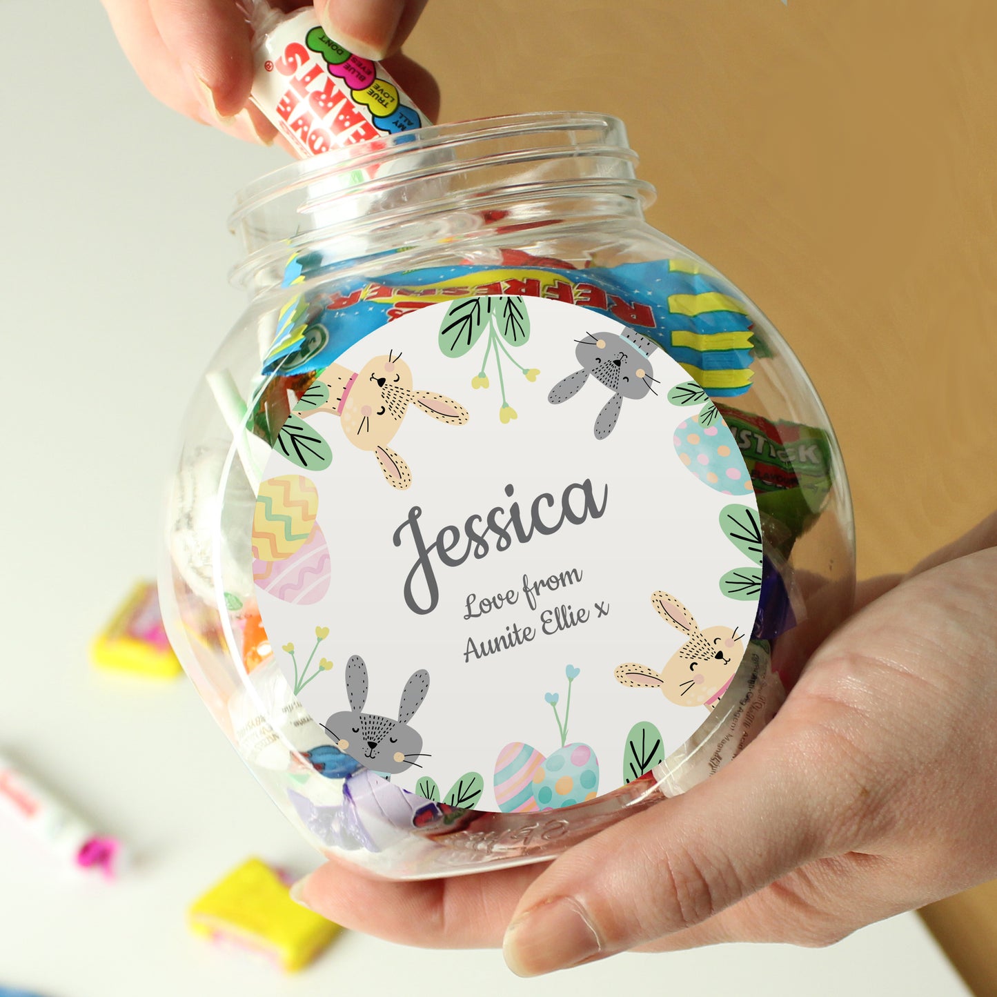 Clear jar with colourful label featuring cartoon animals and text, held by a hand.