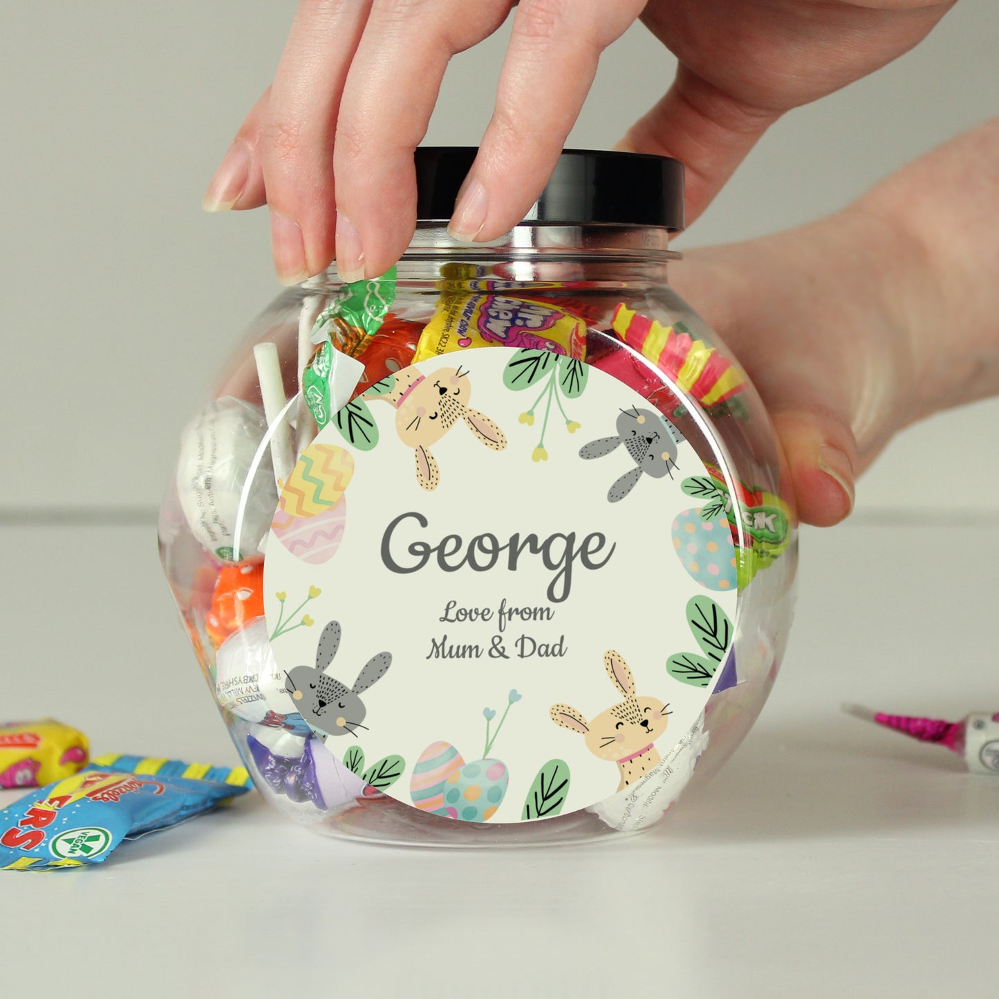 Clear jar with colorful label featuring cartoon animals and text, held by a hand.