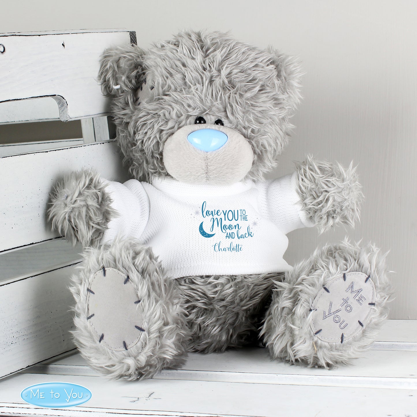 Grey teddy bear with a white shirt displaying text, sitting on a white surface.