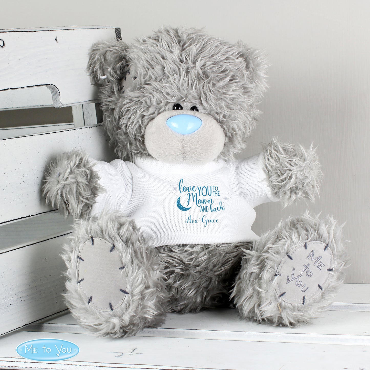 Grey teddy bear with a white shirt displaying text, sitting on a white surface.