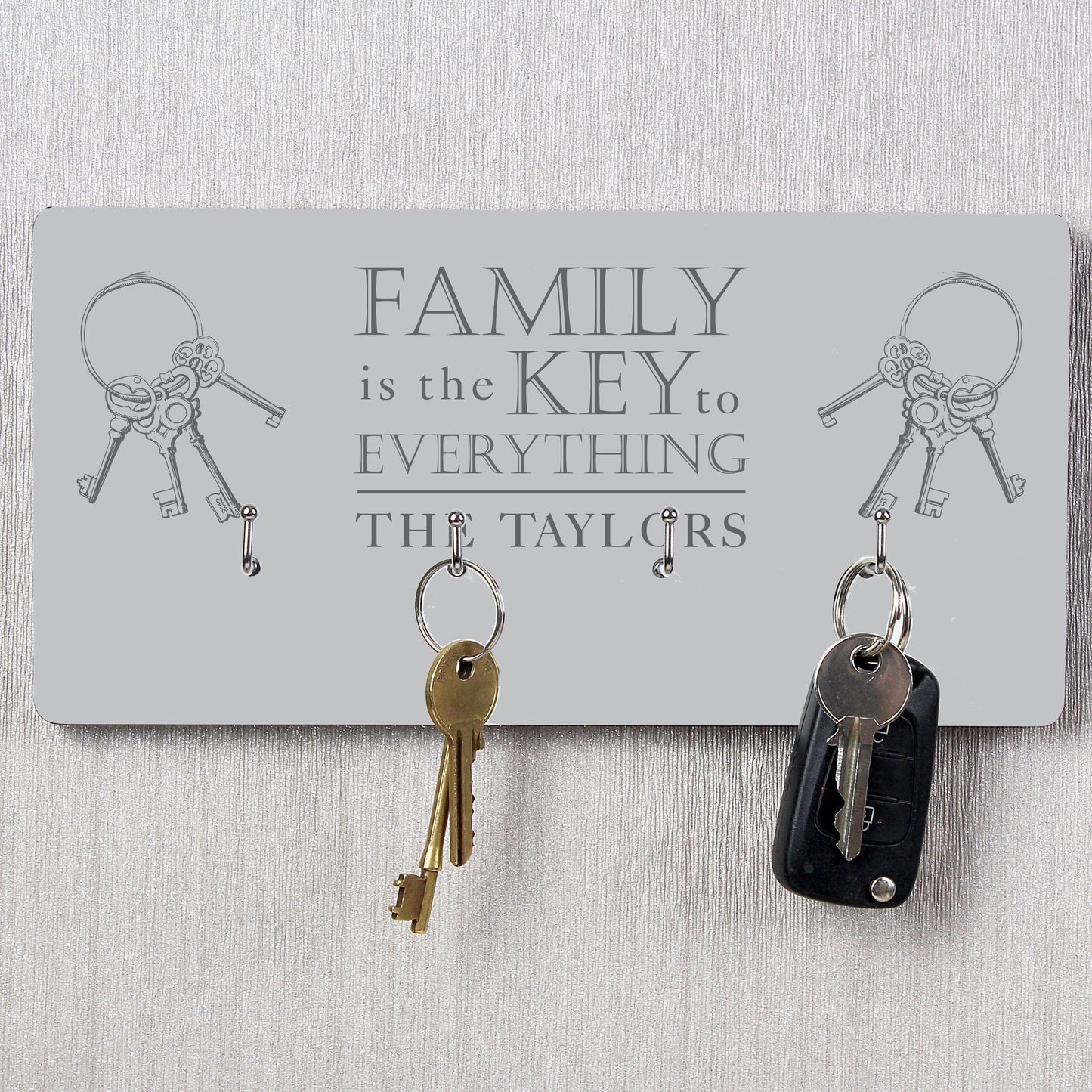 Key holder with keys attached, featuring the text 'Family is the key to everything The Taylors' on a light grey background.