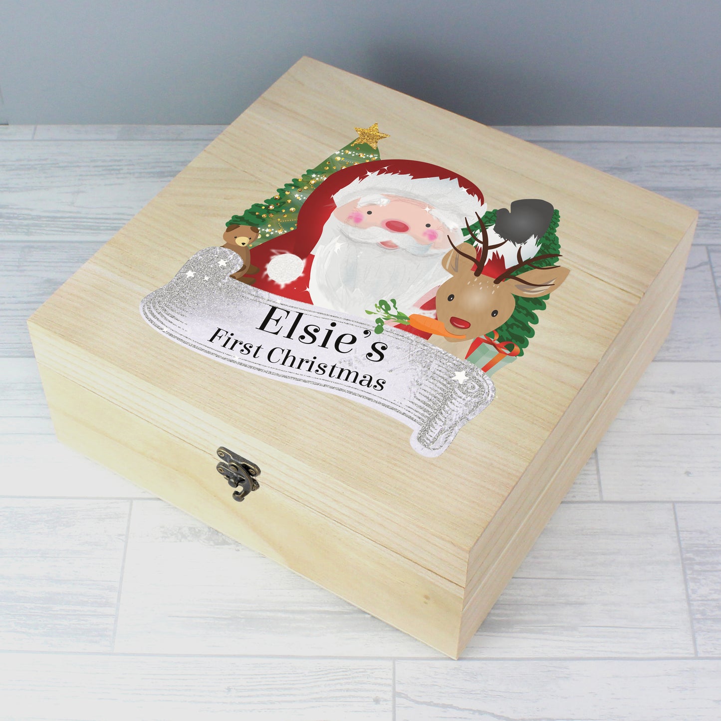 Wooden box with Santa Claus and reindeer design, labeled 'Elsie's First Christmas', on a light wooden surface.