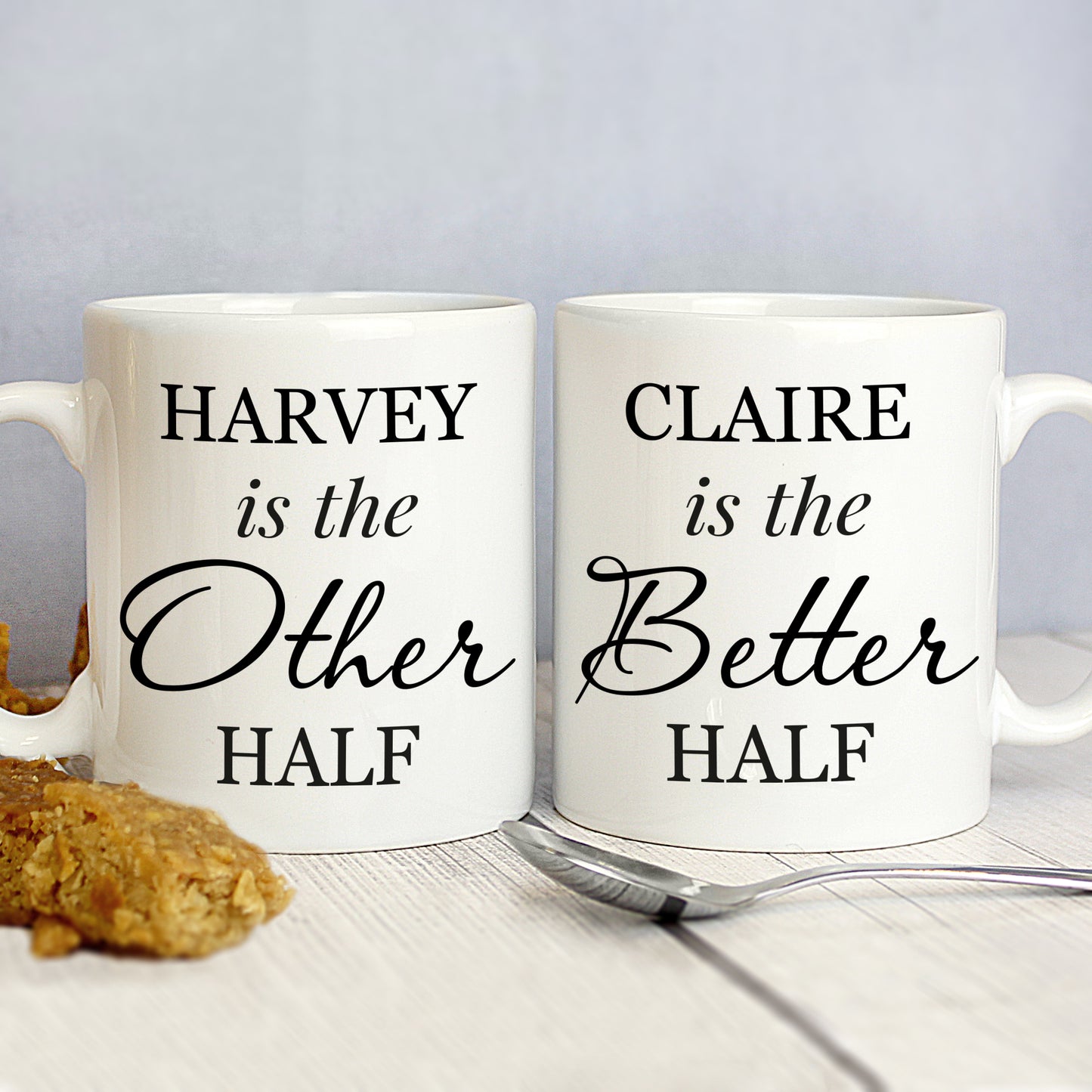 Two white mugs with text on a light surface