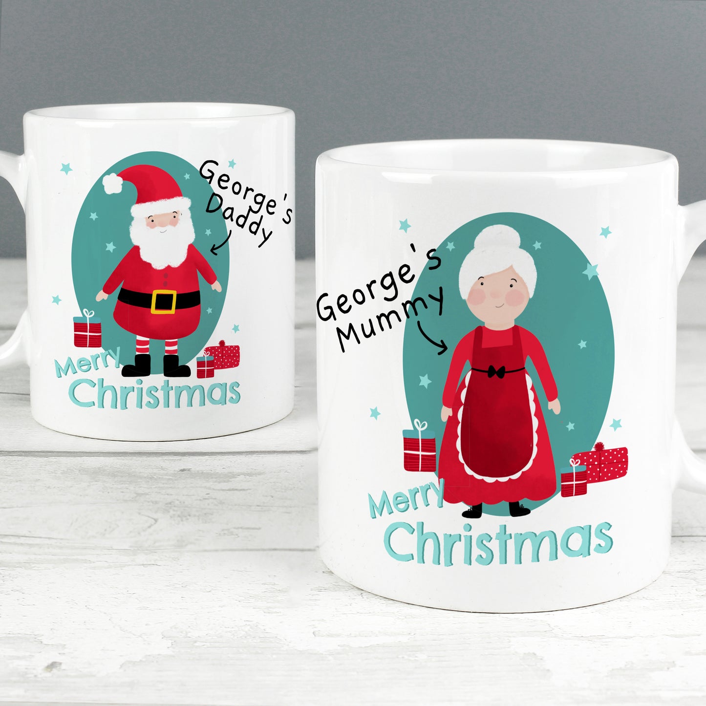 Two Christmas-themed mugs with illustrations of Santa Claus and a woman, labeled 'George's Daddy' and 'George's Mummy', on a white surface.