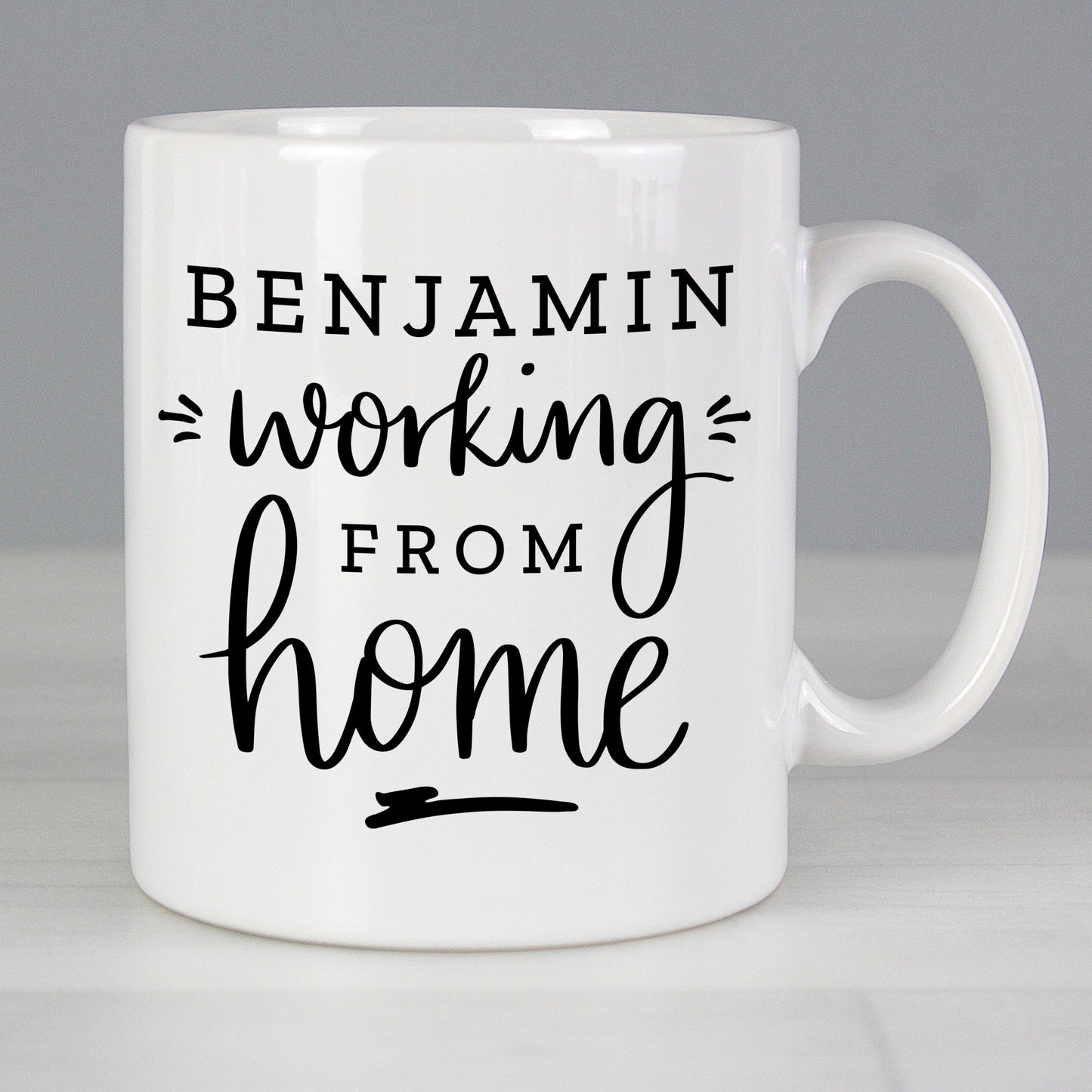 White mug with 'Benjamin working from home' text on a gray background