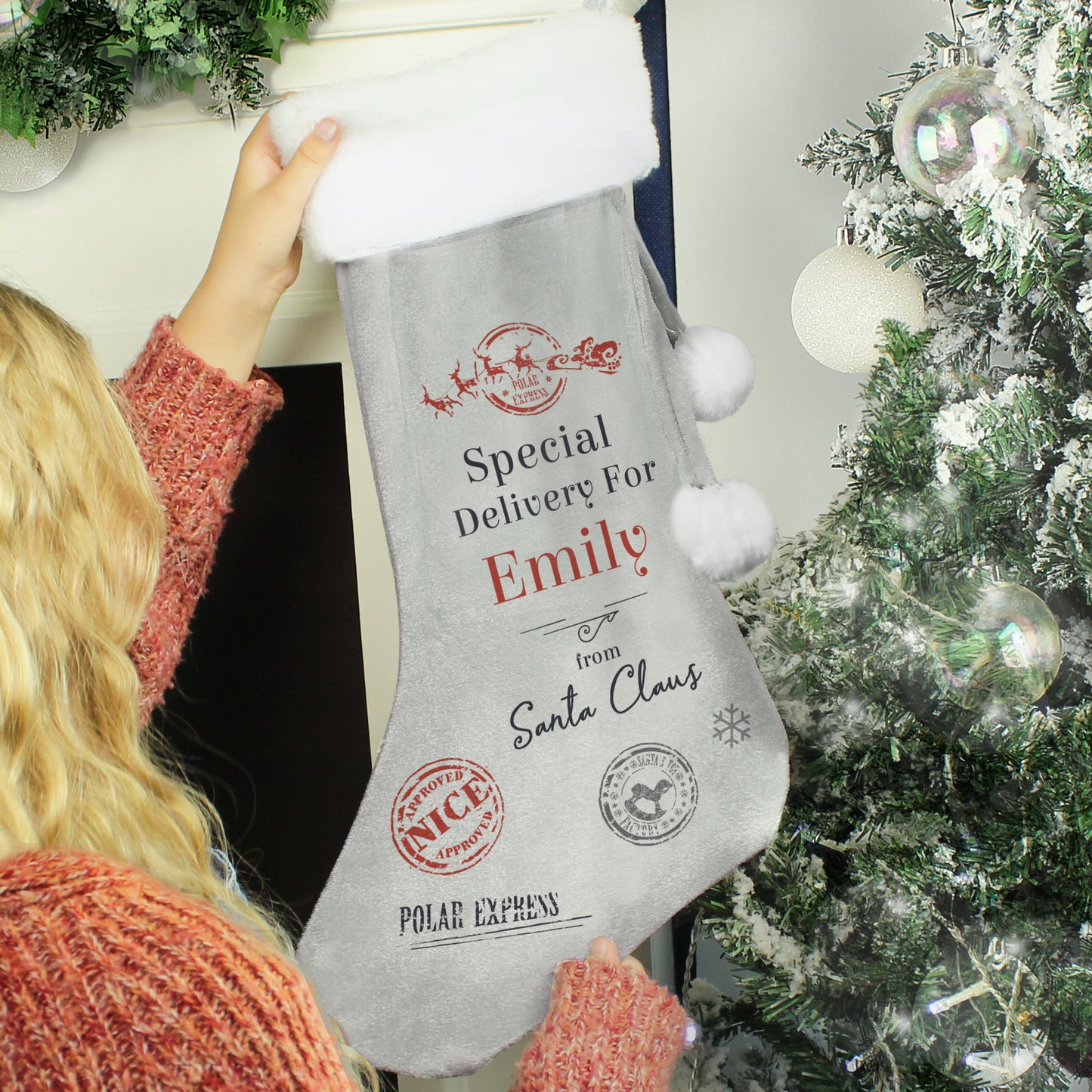 Person holding a personalised Christmas stocking with festive text in front of a decorated tree.