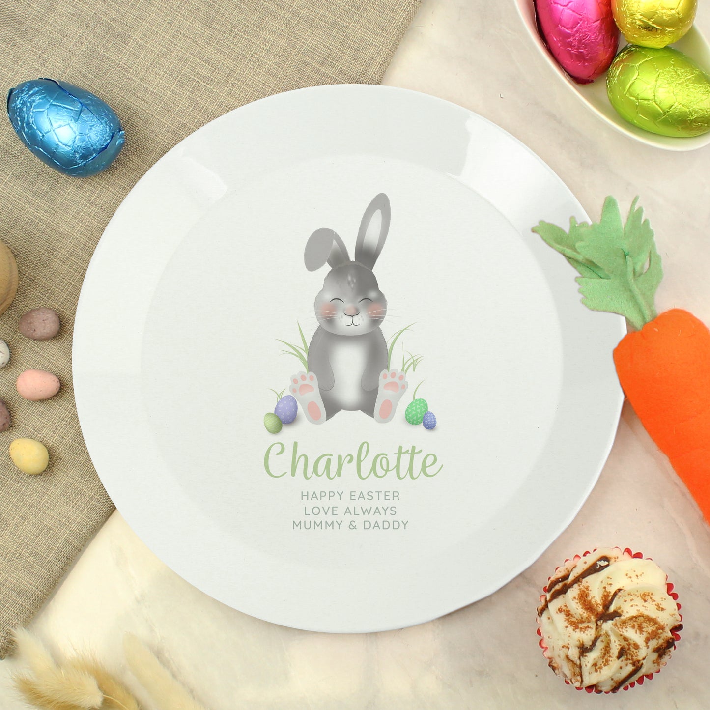 White plate with an Easter bunny design and personalised text, surrounded by Easter decorations.