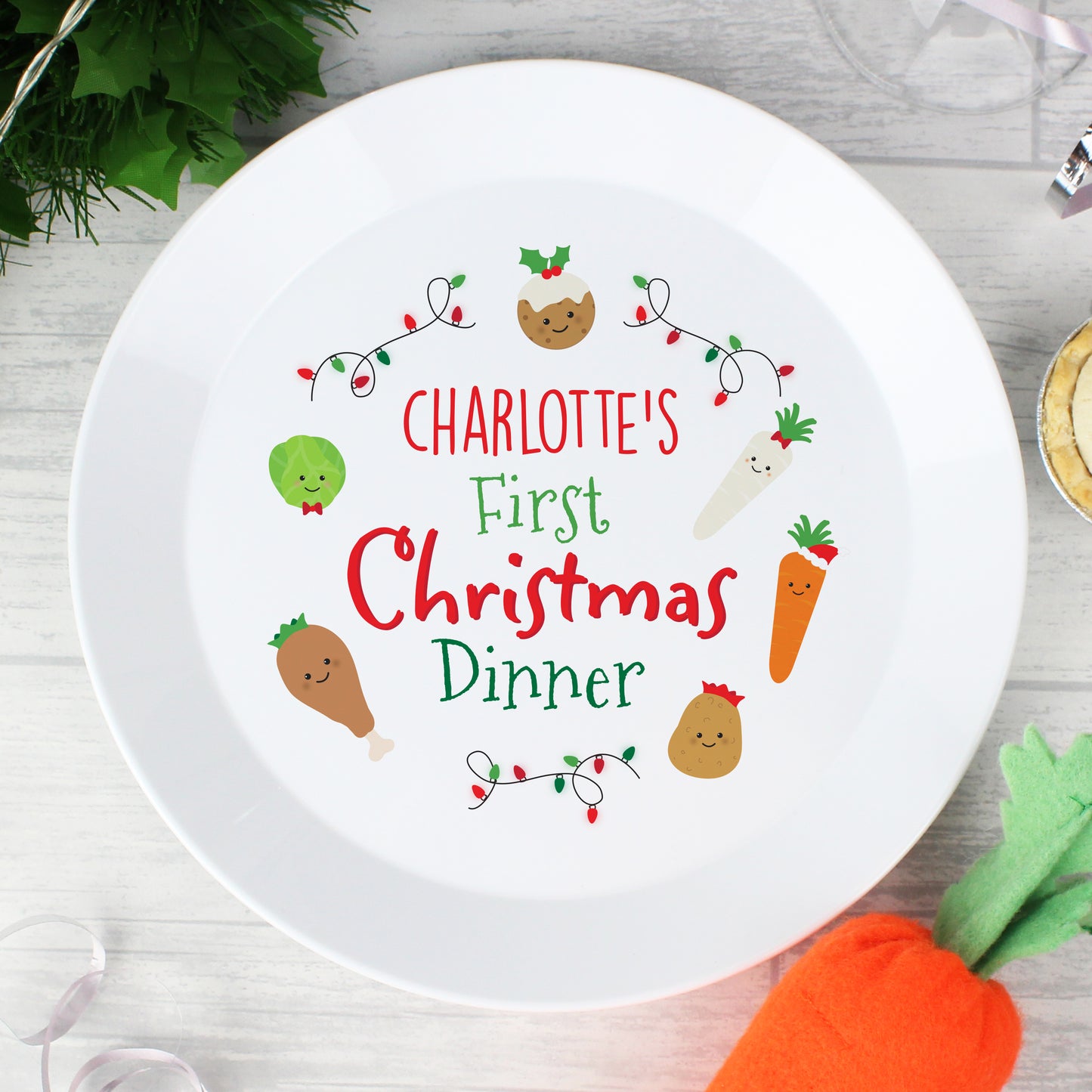White plate with 'Charlotte's First Christmas Dinner' text and festive illustrations on a wooden surface.