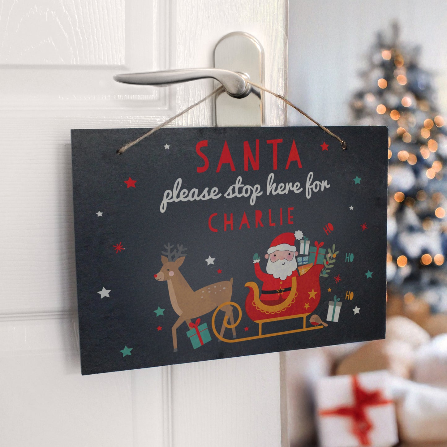 Decorative sign with Santa Claus and reindeer on a door handle, Christmas tree in the background