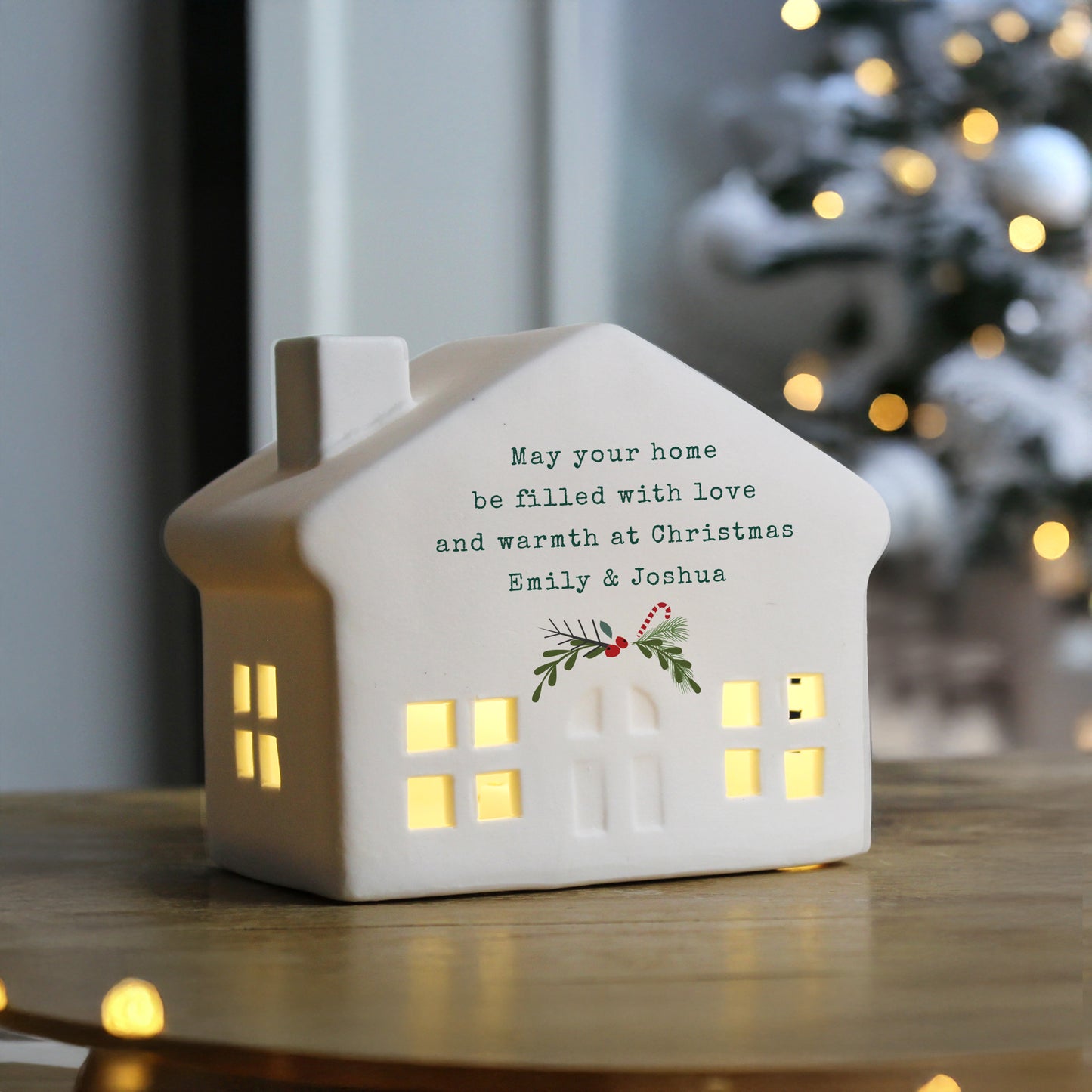 Decorative house-shaped night light with Christmas message and tree in the background