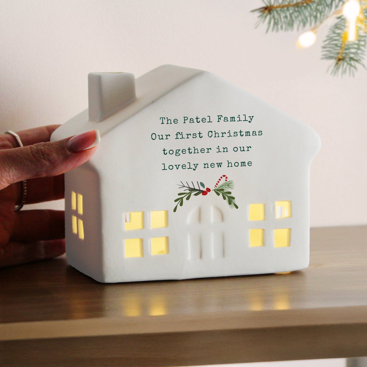 White house-shaped light with personalised message on a wooden surface with Christmas decorations.