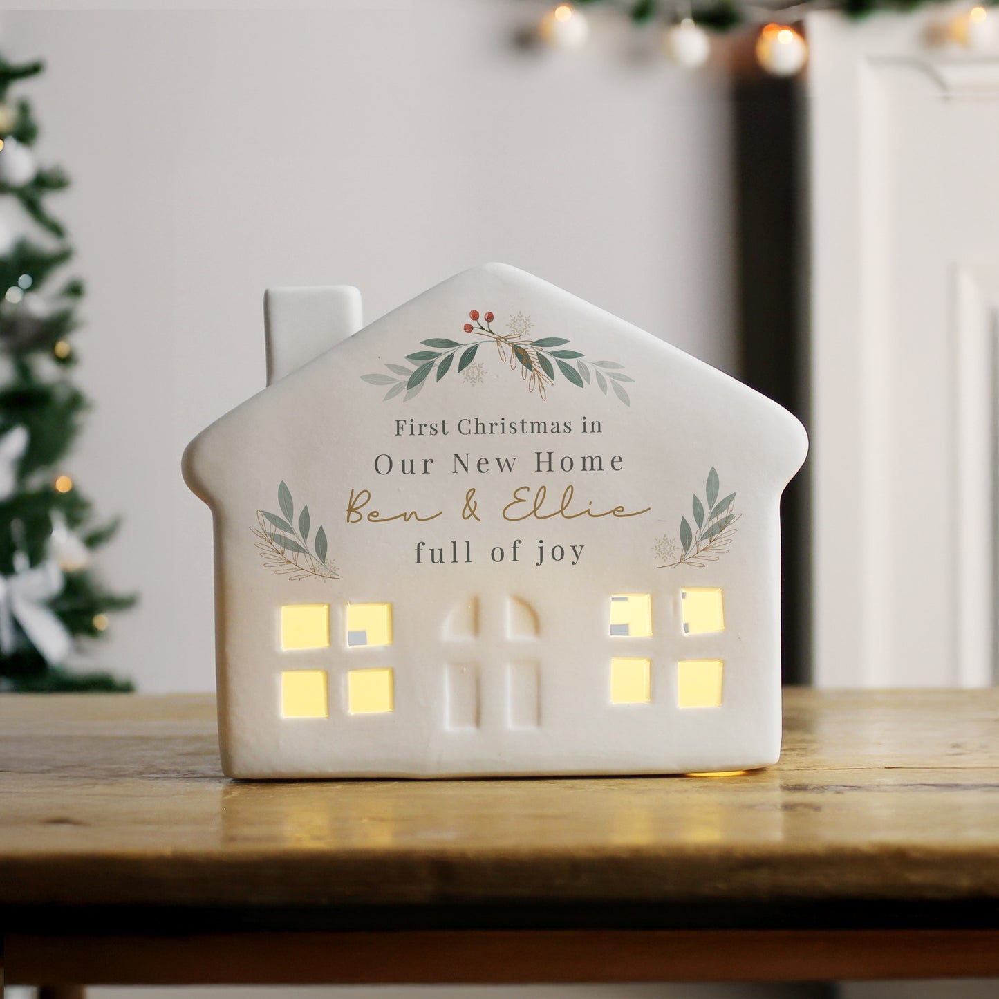 House-shaped light with personalised text on a wooden table, Christmas tree in the background