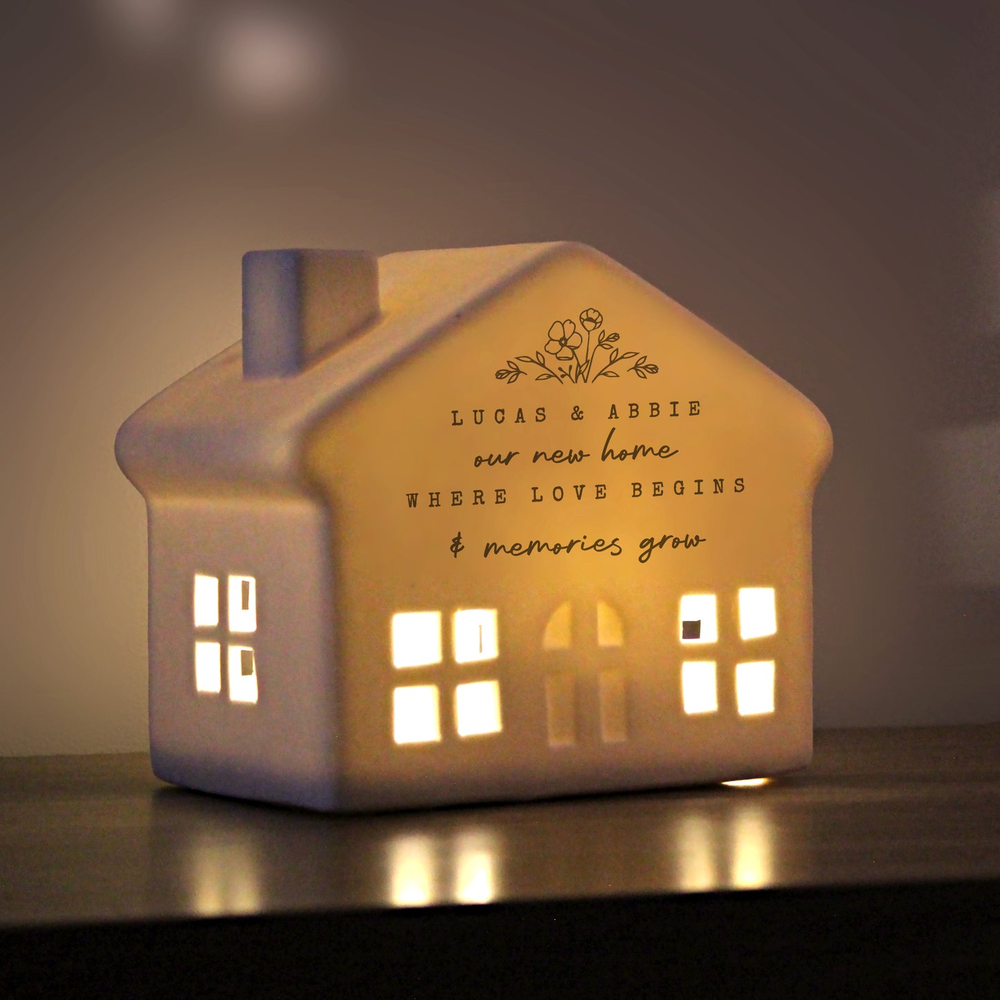 Ceramic house-shaped light with engraved text on a dark background