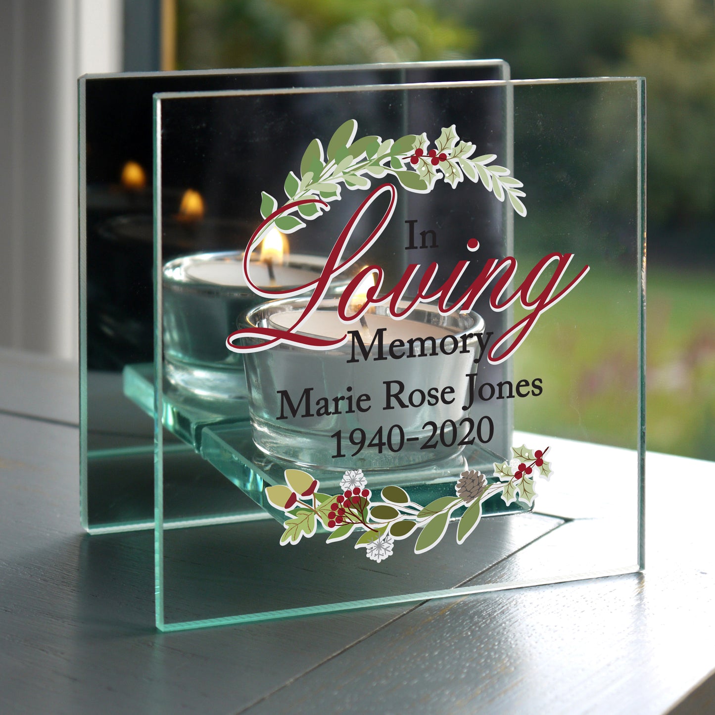 Memorial glass with candles and personalized text on a reflective surface.