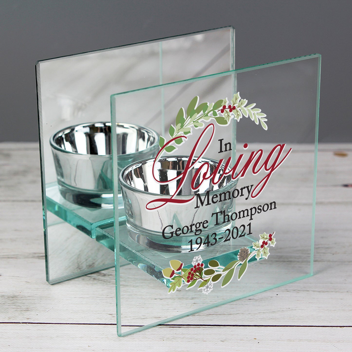 Glass memorial holder with two silver bowls and engraved text on a wooden surface.