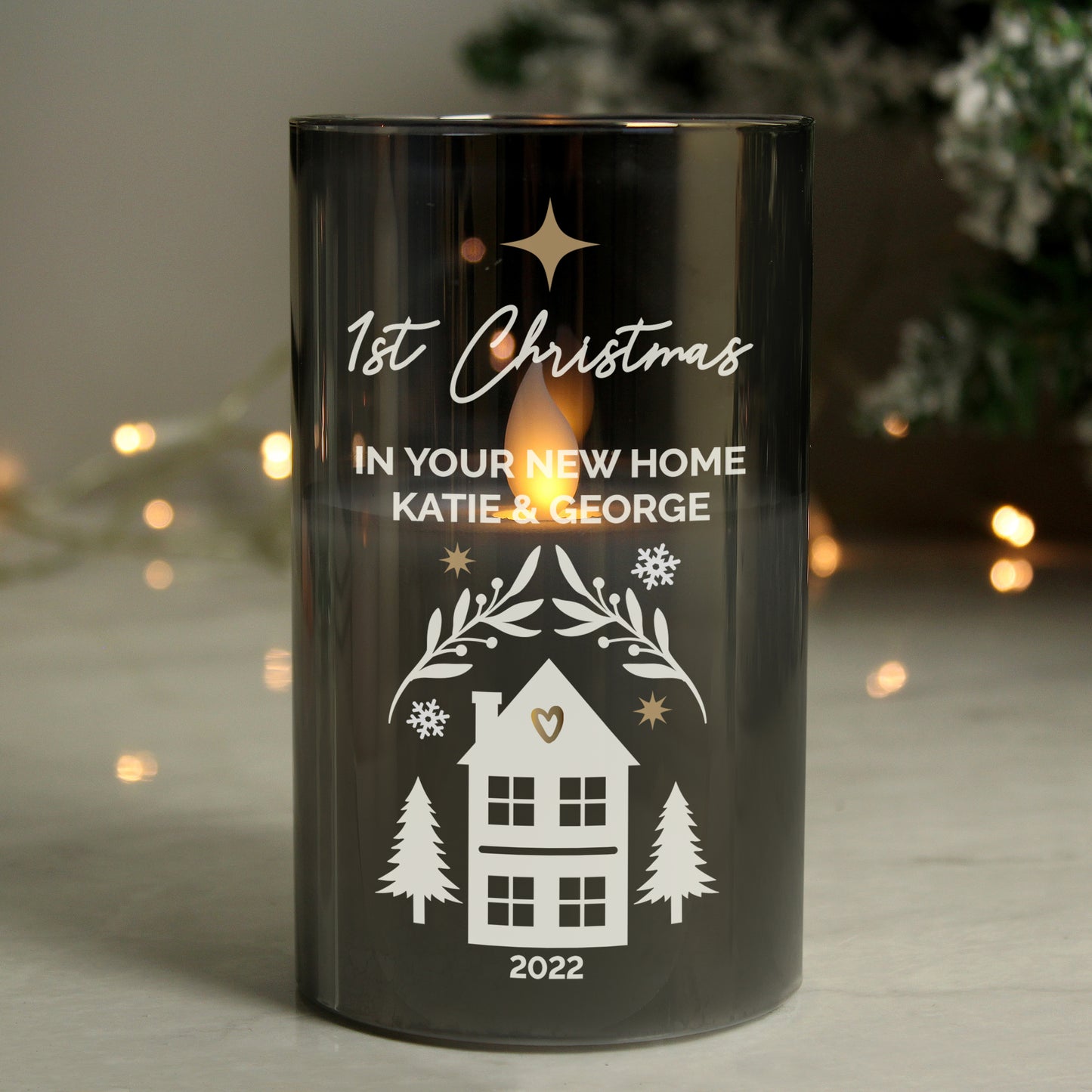Black candle with '1st Christmas in your new home' text and house illustration, set against a blurred festive background.