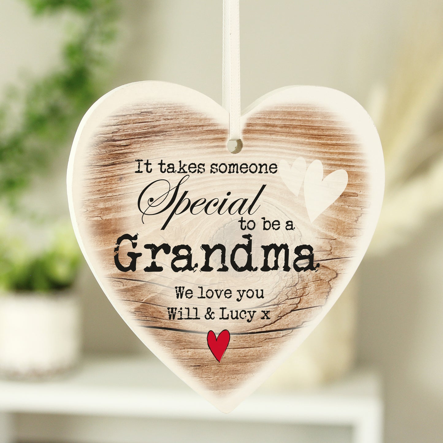 Wooden heart-shaped plaque with printed text and a red heart, hanging against a blurred background.