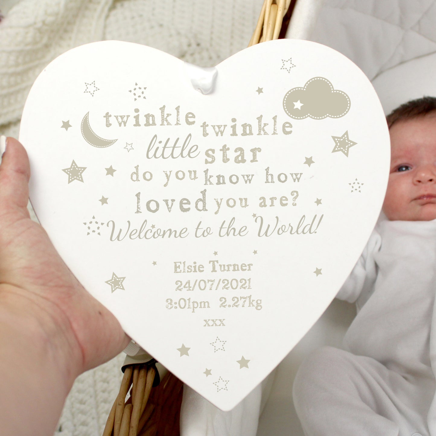 Heart-shaped decorative plaque with engraved text about a newborn baby held by a person.