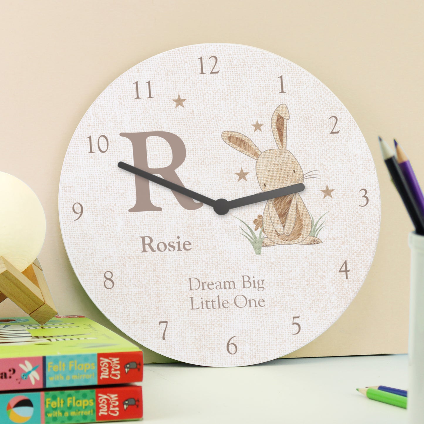 Children's wall clock with a rabbit illustration and personalised text, placed on a surface with stationery items.