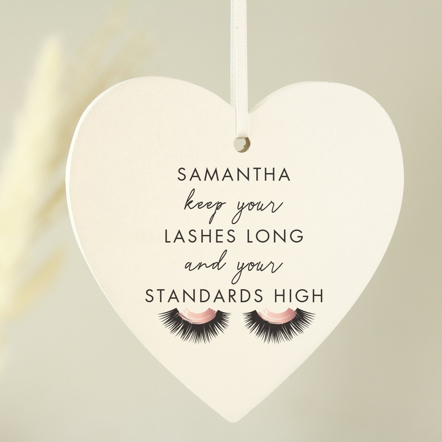 Heart-shaped hanging sign with eyelashes and personalised name on a neutral background