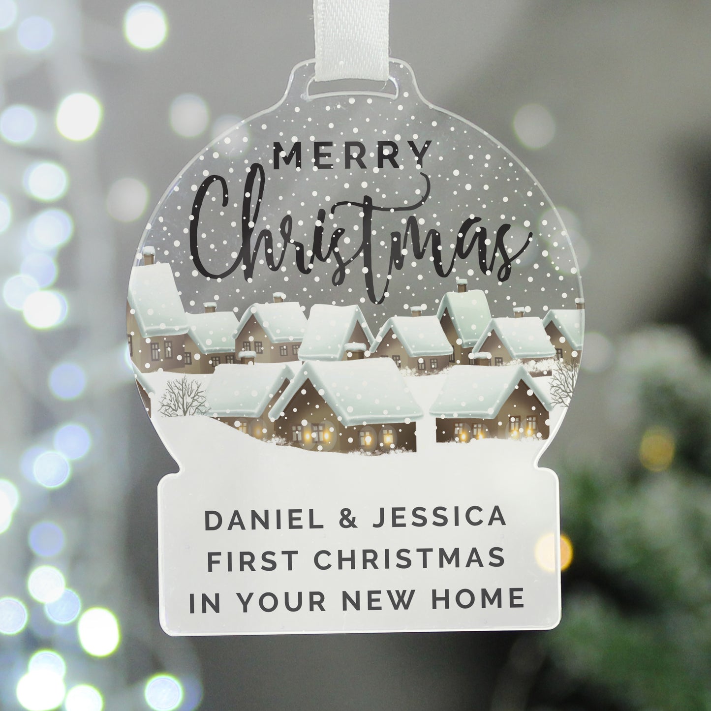 Personalized Christmas ornament with 'Merry Christmas' and house illustration, against a blurred festive background.
