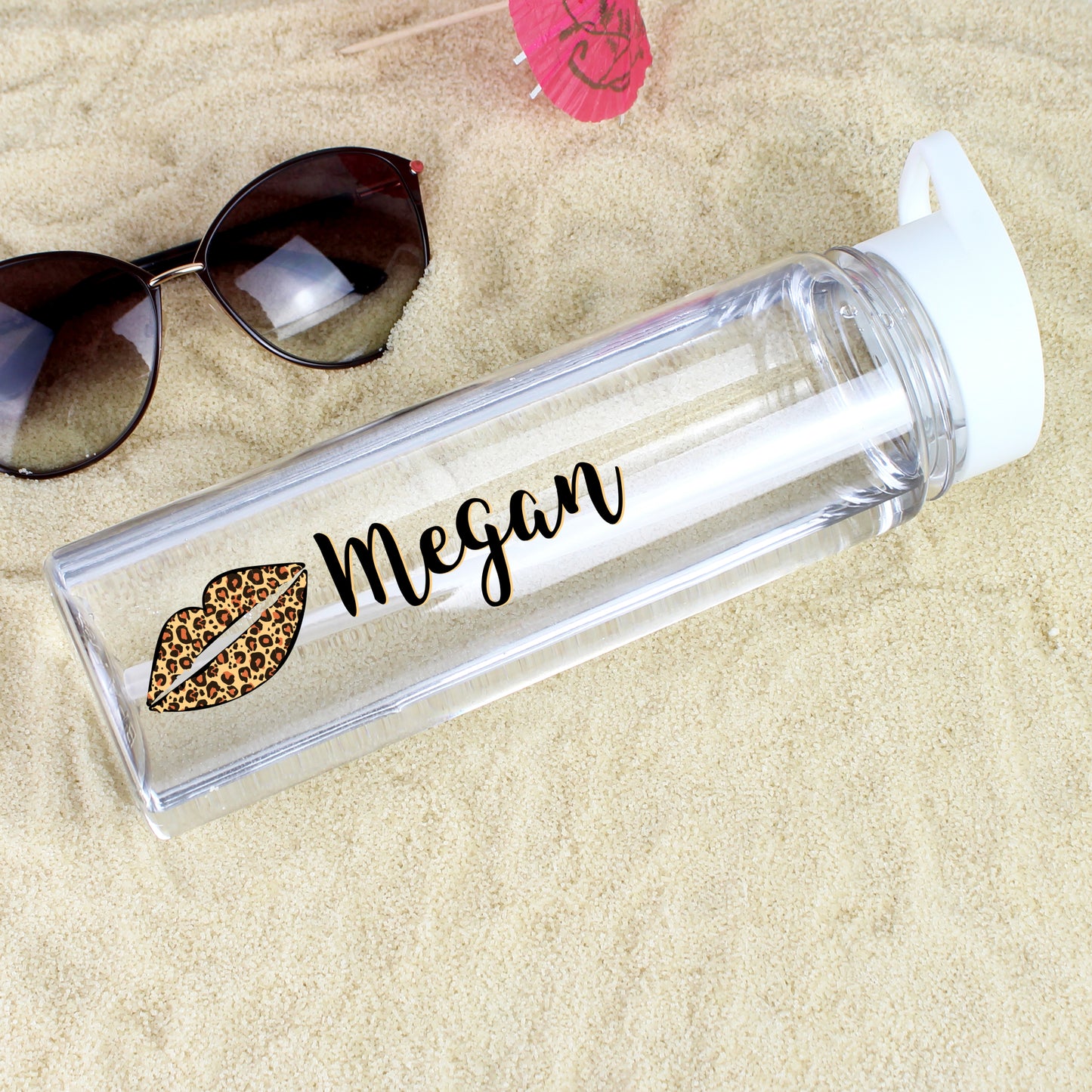Clear water bottle with leopard print lips and 'Megan' on sand with sunglasses