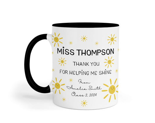 A white ceramic mug with a black handle and interior, decorated with cheerful yellow sun illustrations. The mug reads: "MISS THOMPSON, THANK YOU FOR HELPING ME SHINE. From Amelia Smith, Class 2, 2024."