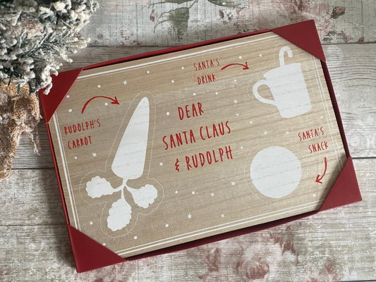 Wooden Christmas Eve board in a red gift box, labeled with festive white illustrations and red text showing spots for 'Rudolph's Carrot,' 'Santa's Drink,' and 'Santa's Snack,' with 'Dear Santa Claus & Rudolph' written in the center