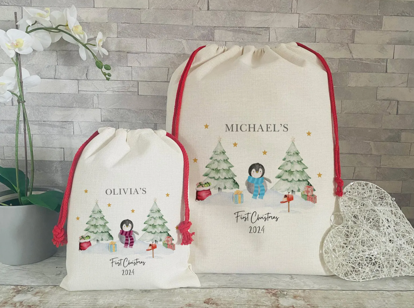 Personalised Christmas gift sacks with penguin and tree design – small sack for Olivia and large sack for Michael, both with red drawstrings and 'First Christmas 2024' printed below