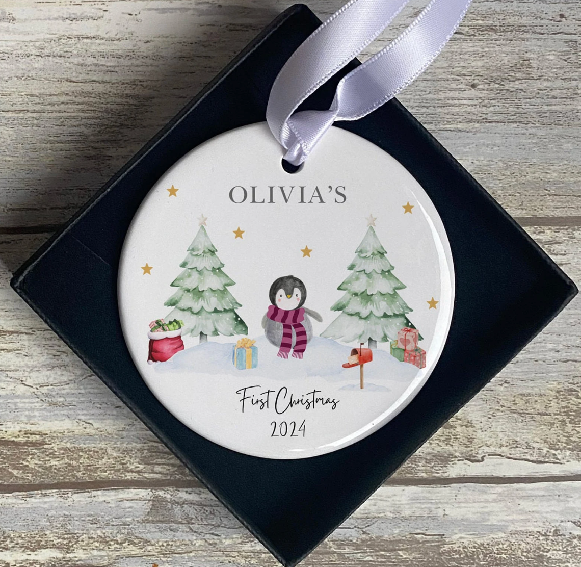 Custom Christmas tree ornament with penguin design, presents, and snow-covered trees. Text reads “Olivia’s First Christmas 2024.” A thoughtful personalised gift or festive keepsake for children, babies, or toddlers celebrating their first holiday season.