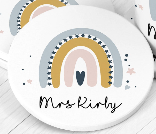 Round ceramic teacher coaster with rainbow design and 'Mrs Kirly' text on a white surface