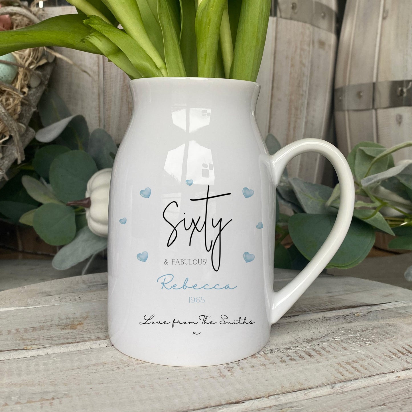 Personalised ceramic jug with 'Sixty & Fabulous' design, blue heart accents, and custom name and message, used as a vase for flowers