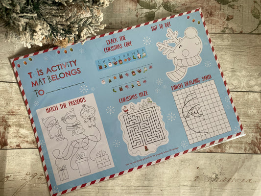 A colourful Christmas-themed children's activity mat with various fun games printed on a light blue background. The mat includes sections like “This activity mat belongs to,” “Crack the Christmas Code,” “Dot to Dot,” “Finish Drawing Santa,” “Christmas Maze,” and “Match the Presents.” Surrounded by candy cane stripe borders, the mat is filled with festive illustrations such as Santa, elves, a reindeer, and snowflakes. A perfect holiday entertainment item for young children.