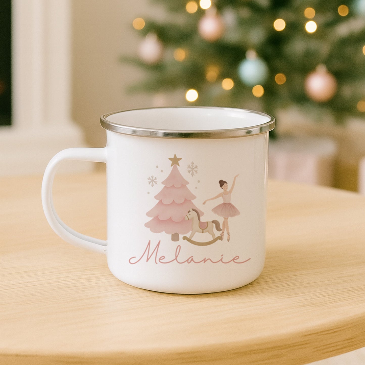 White mug with Christmas design and 'Melanie' text on a wooden table with a decorated Christmas tree in the background.