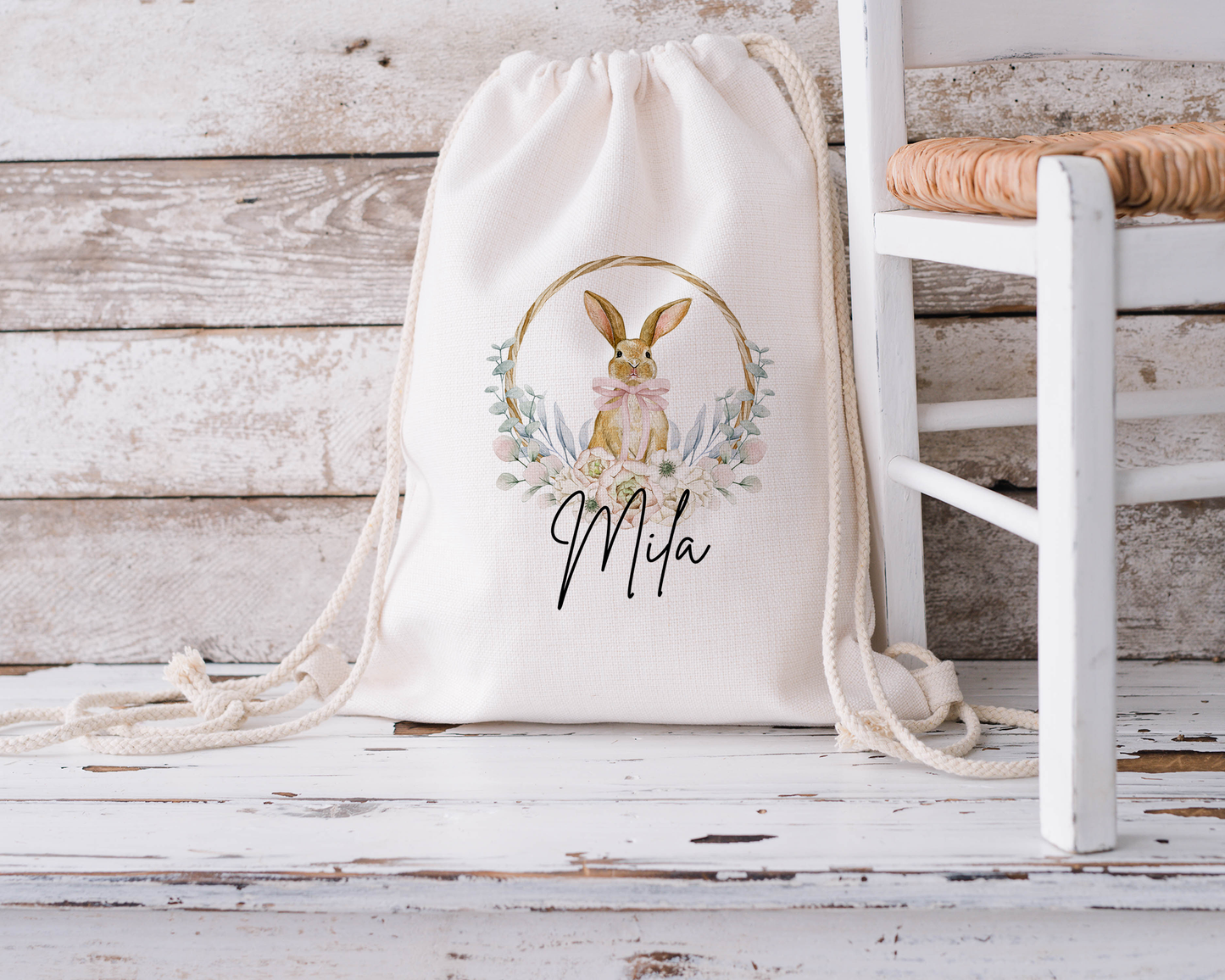 Personalised children's Easter bunny drawstring bag featuring a cute floral bunny design and custom name "Mila" on a rustic wooden background. Ideal for Easter egg hunts or gift giving.