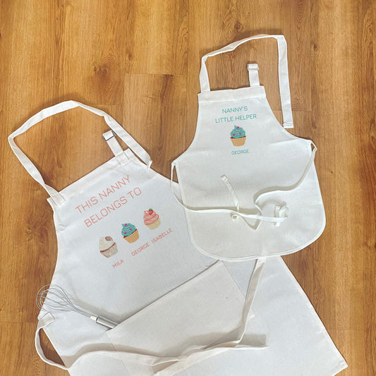 Personalised apron set for nanny and child – white aprons featuring cute cupcake designs and custom names, ideal baking gift for grandma and grandchildren.