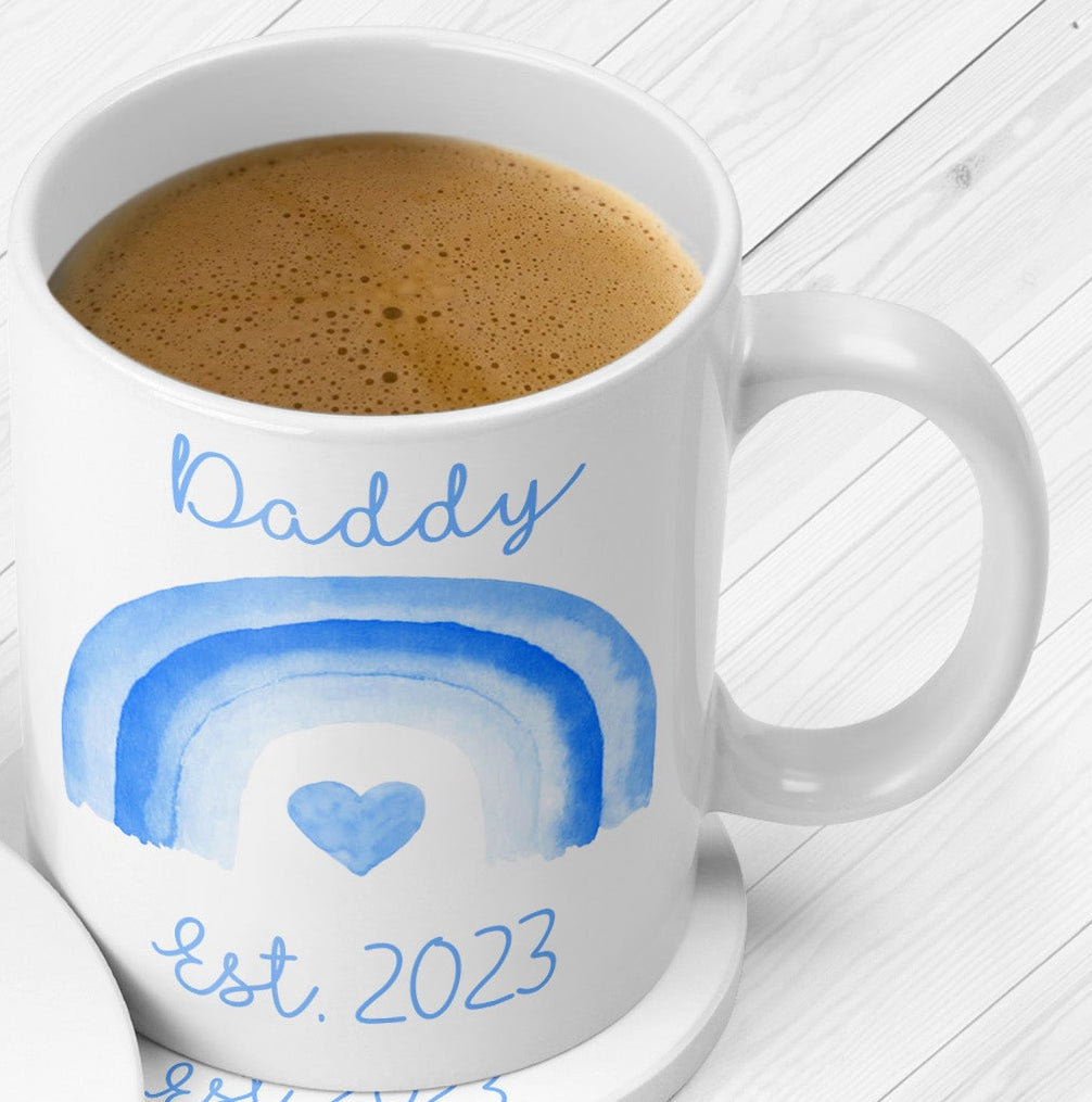 White mug with blue rainbows and text on a white wooden surface.