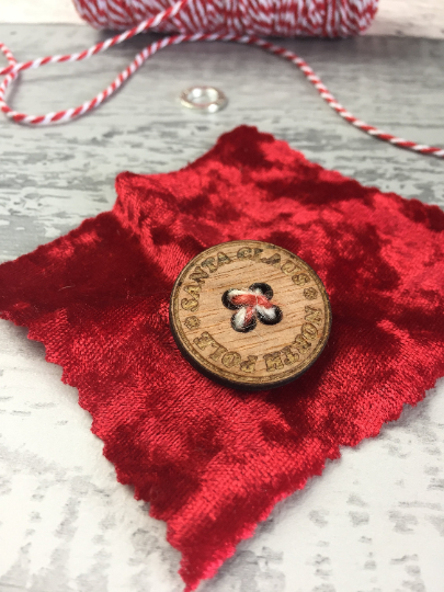 Red fabric with a wooden Santa button on a grey surface.