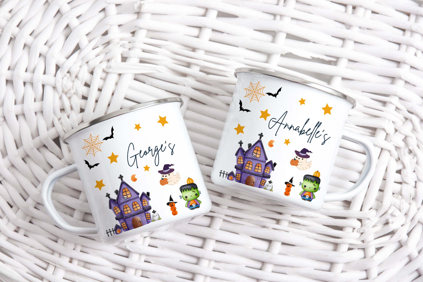 Two Halloween-themed enamel mugs with personalised names on a wicker surface