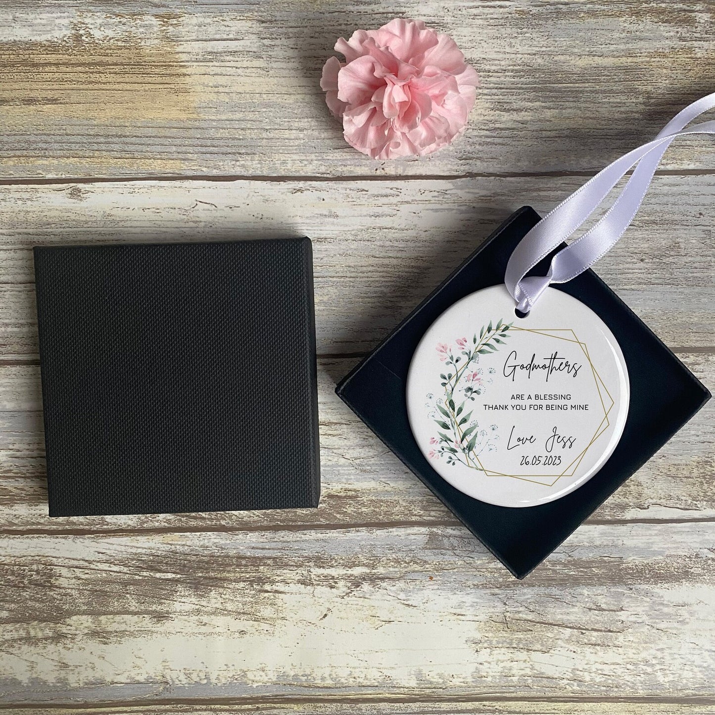 Overhead shot of the boxed ornament and black lid on rustic wooden background with a pink carnation at the top.