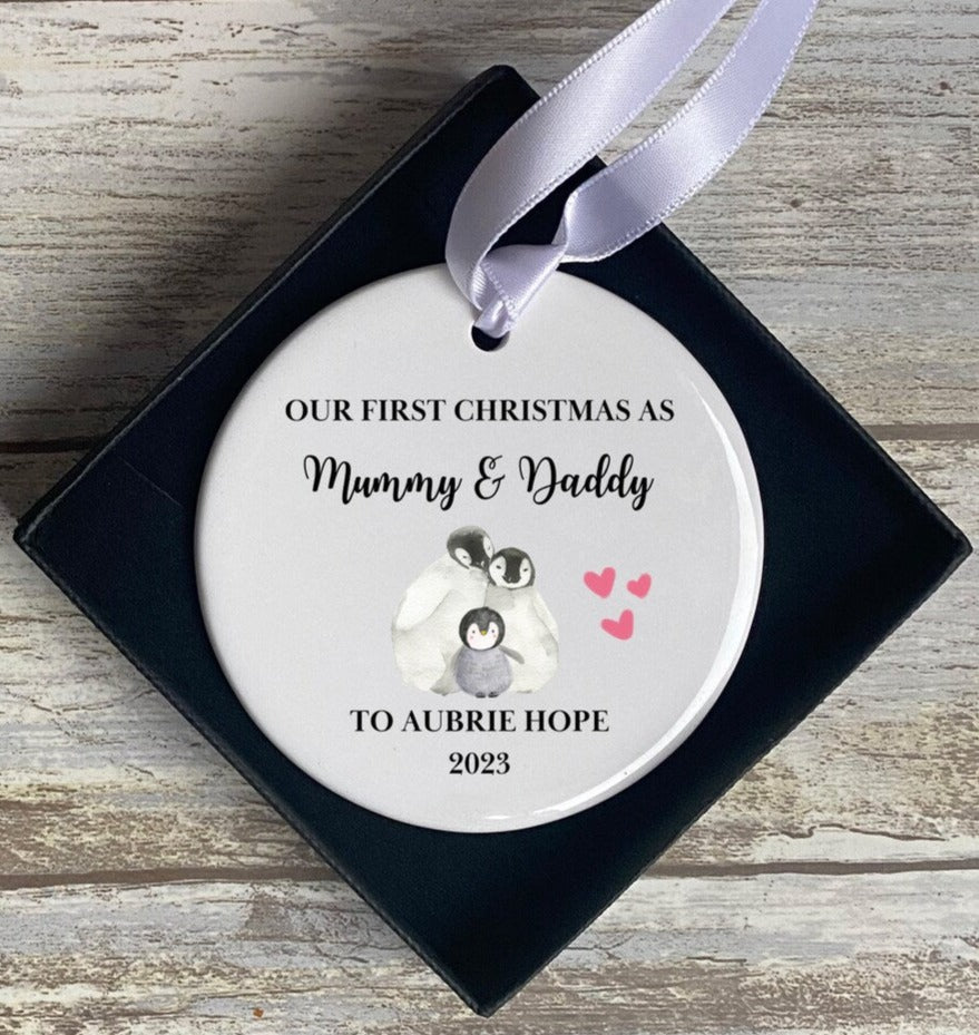 Personalised 'Our First Christmas as Mummy & Daddy' ceramic bauble with penguin family illustration, pink hearts, baby's name 'Aubrie Hope' and 2023 date – sentimental gift keepsake for new parents' first Christmas