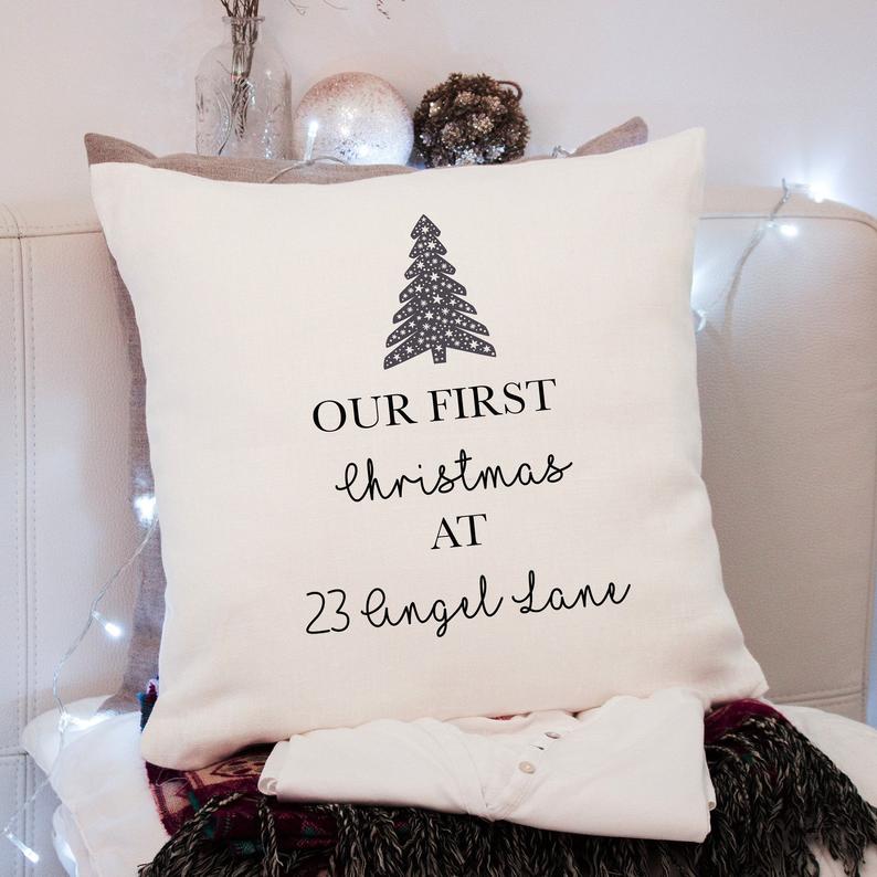 Personalised Decorative cushion with 'Our First Christmas at 23 Angel Lane' text and Christmas tree design on a couch.