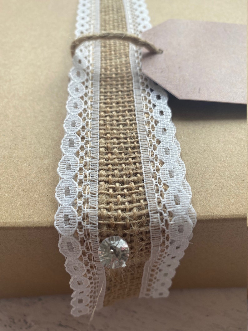 Roll of burlap ribbon with lace trim on a neutral background