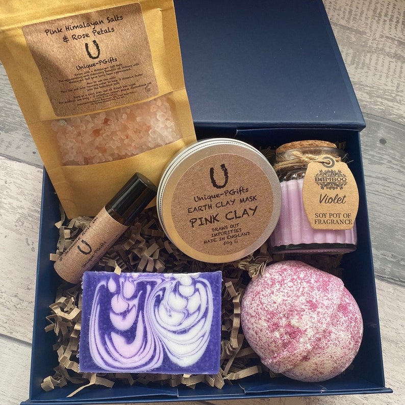 Collection of self-care products including a pink clay mask, bath bomb, and soap in a blue box.