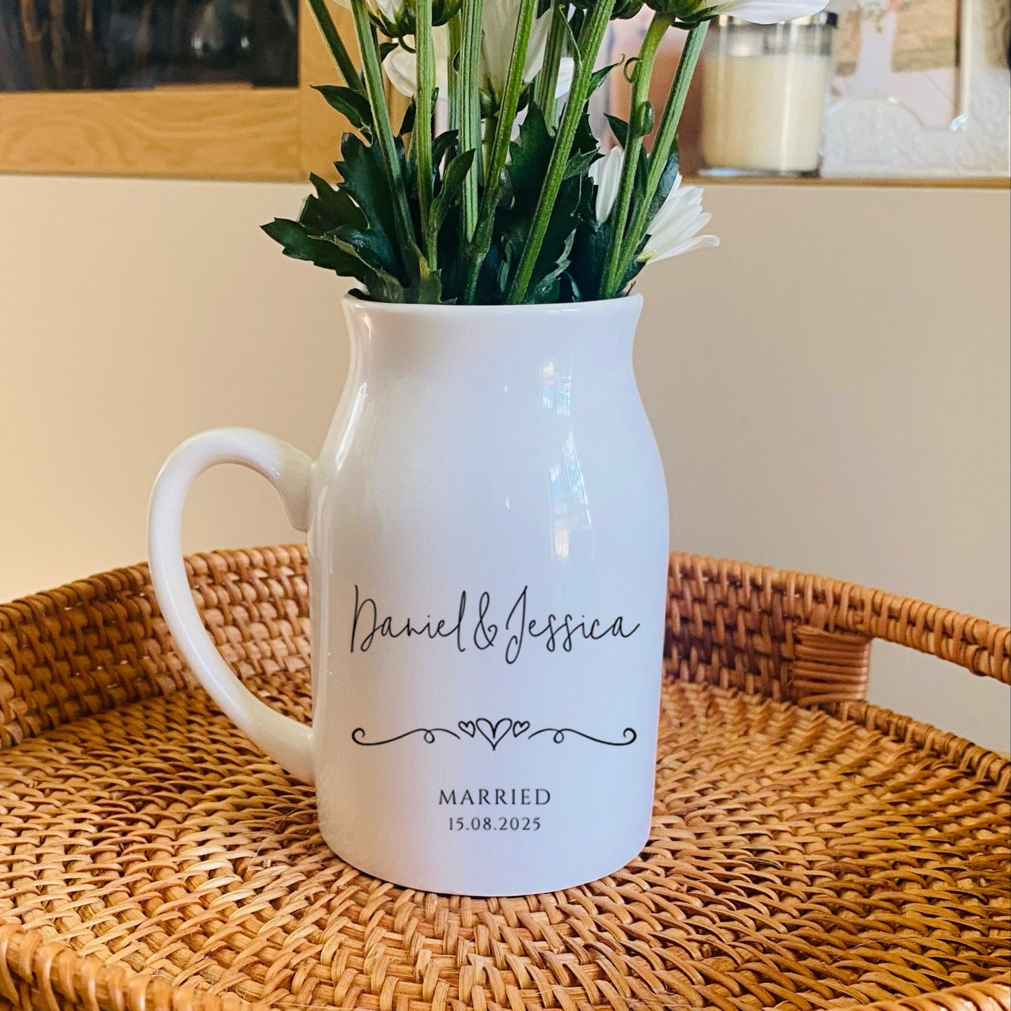 Personalised Wedding Vase. White pitcher with floral arrangement on a woven tray in a home setting