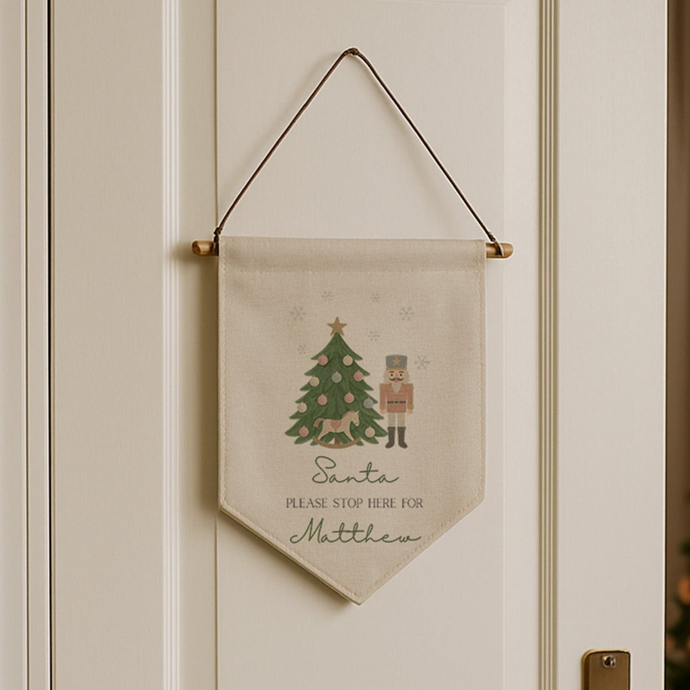 Decorative Christmas banner hanging on a door with a Christmas tree in the background.