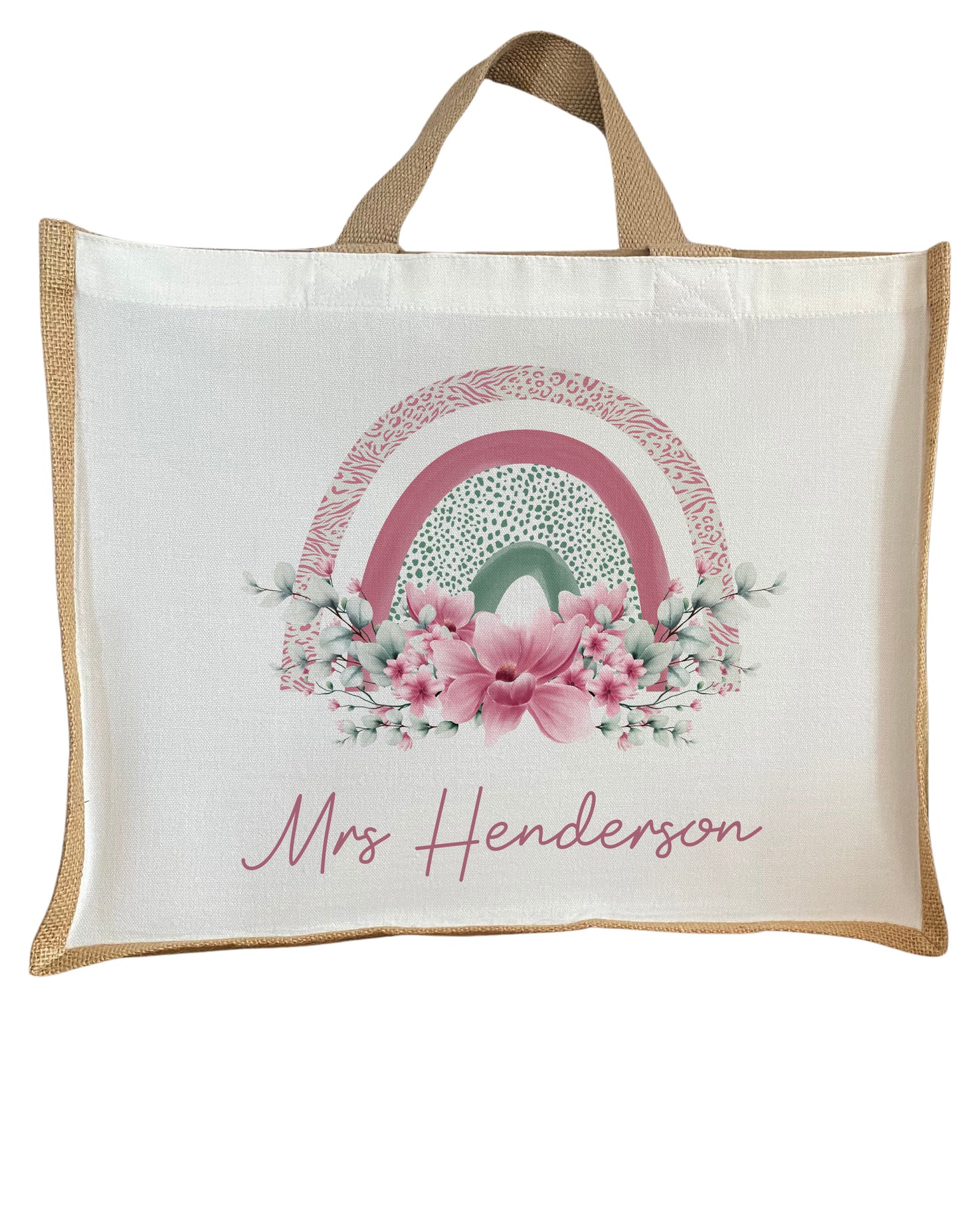 Personalised jute tote bag featuring the name "Mrs Henderson" in elegant pink script. The design showcases a pastel pink and green rainbow surrounded by a floral arrangement of pink and white flowers. The bag has natural jute handles and trim, with no external pocket.