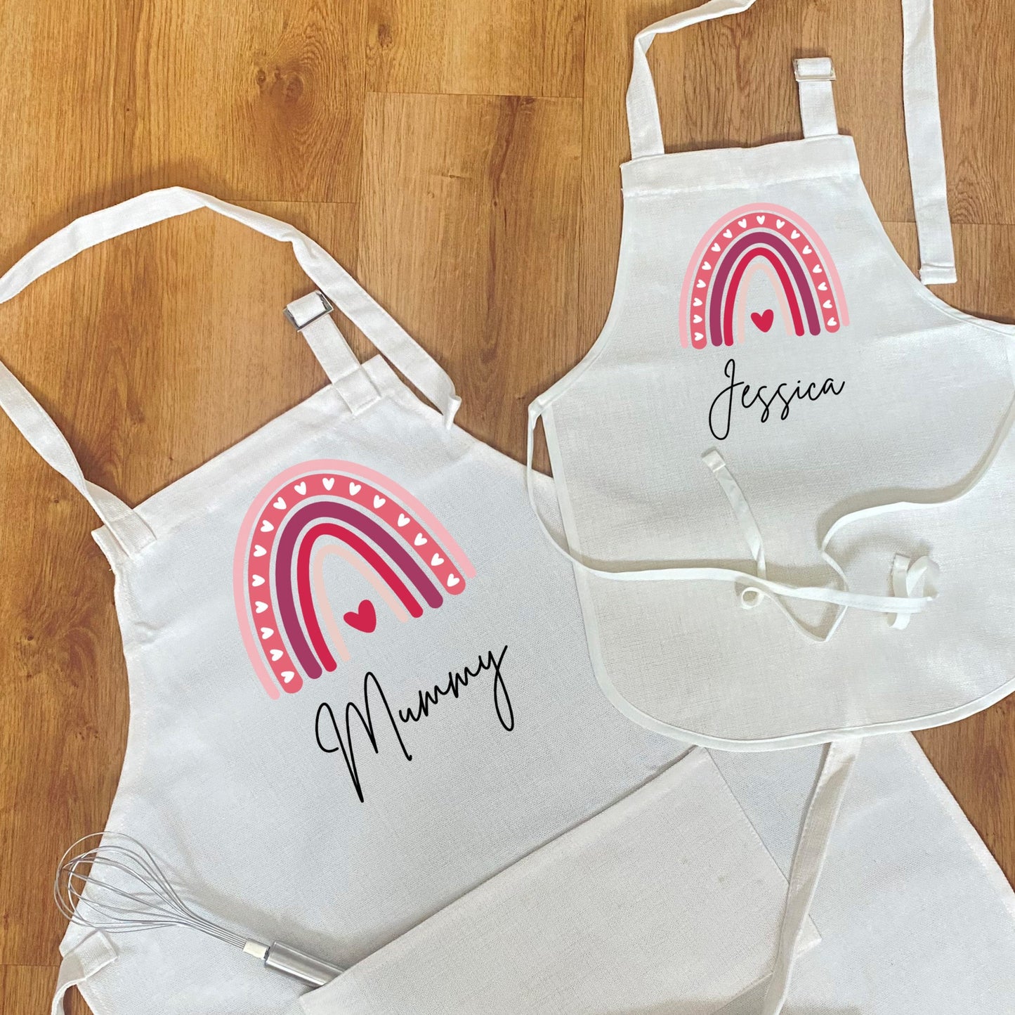 Matching mother and child personalised aprons – white cotton aprons with pink rainbow and heart design, custom names ‘Mummy’ and ‘Jessica’, ideal gift for baking or cooking together.