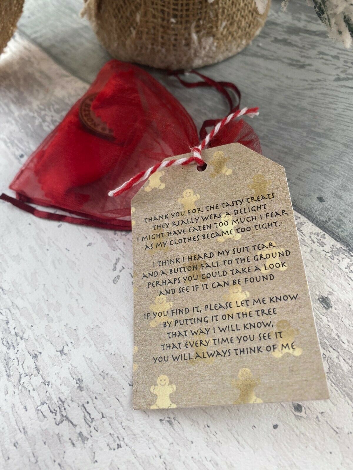 Textile tag with a message on a textured surface with a red bag and gingerbread man decorations.