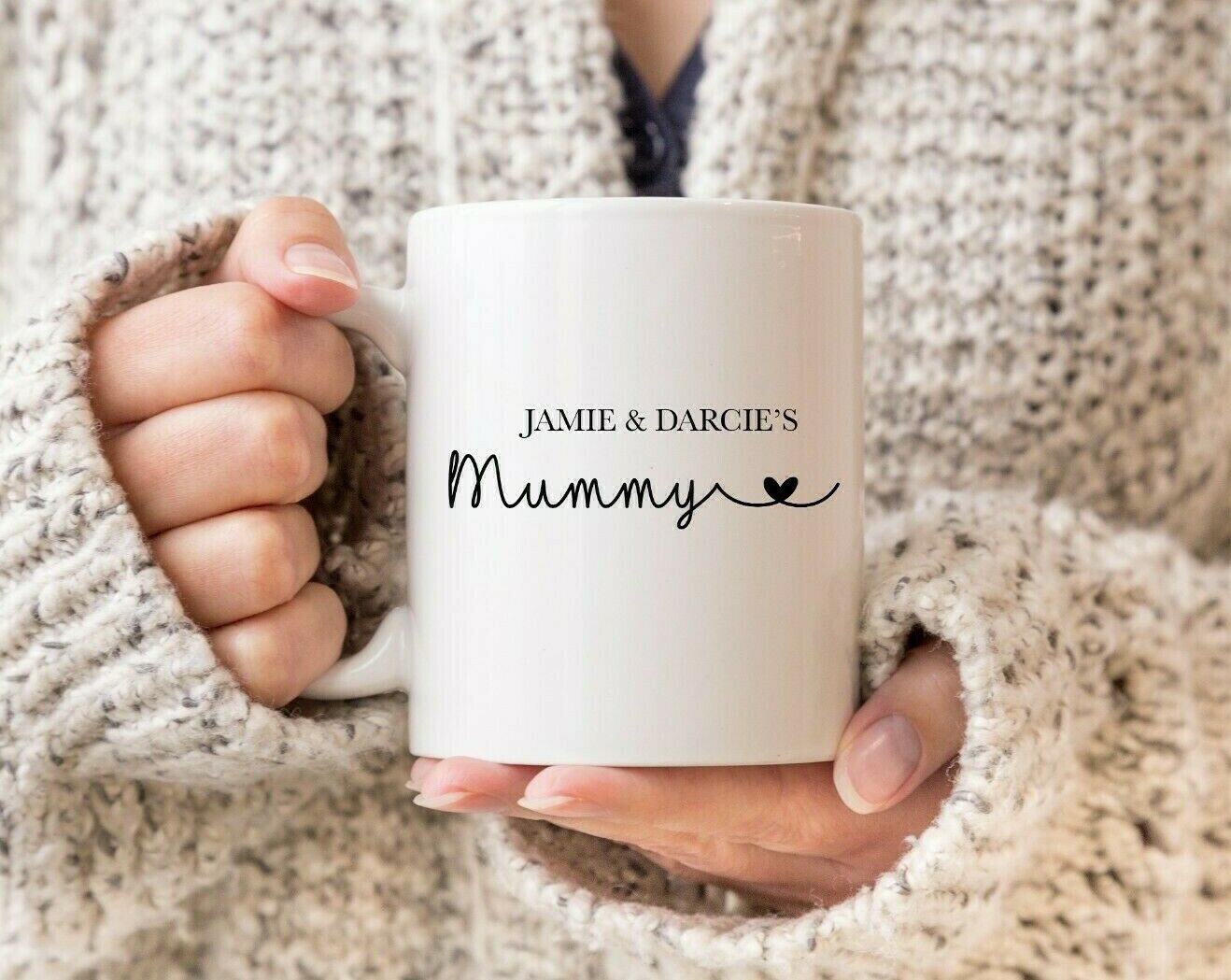 A person holding a white ceramic mug with the personalised text 'Jamie & Darcie's Mummy' printed on it.